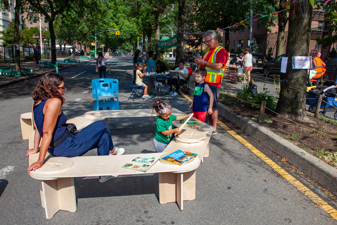 A view of people sitting on a wooden bench on an open street in nyc.