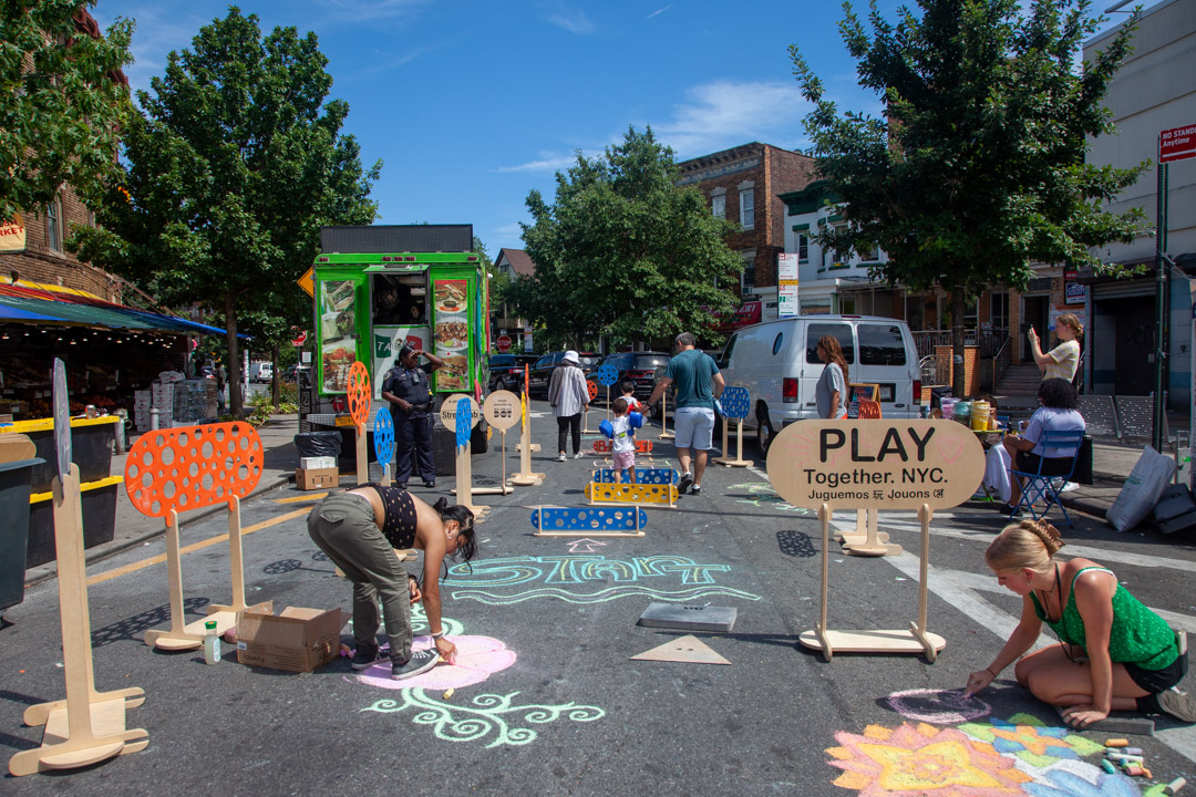 A car-free street with chalk murals and play obstacles on the ground.