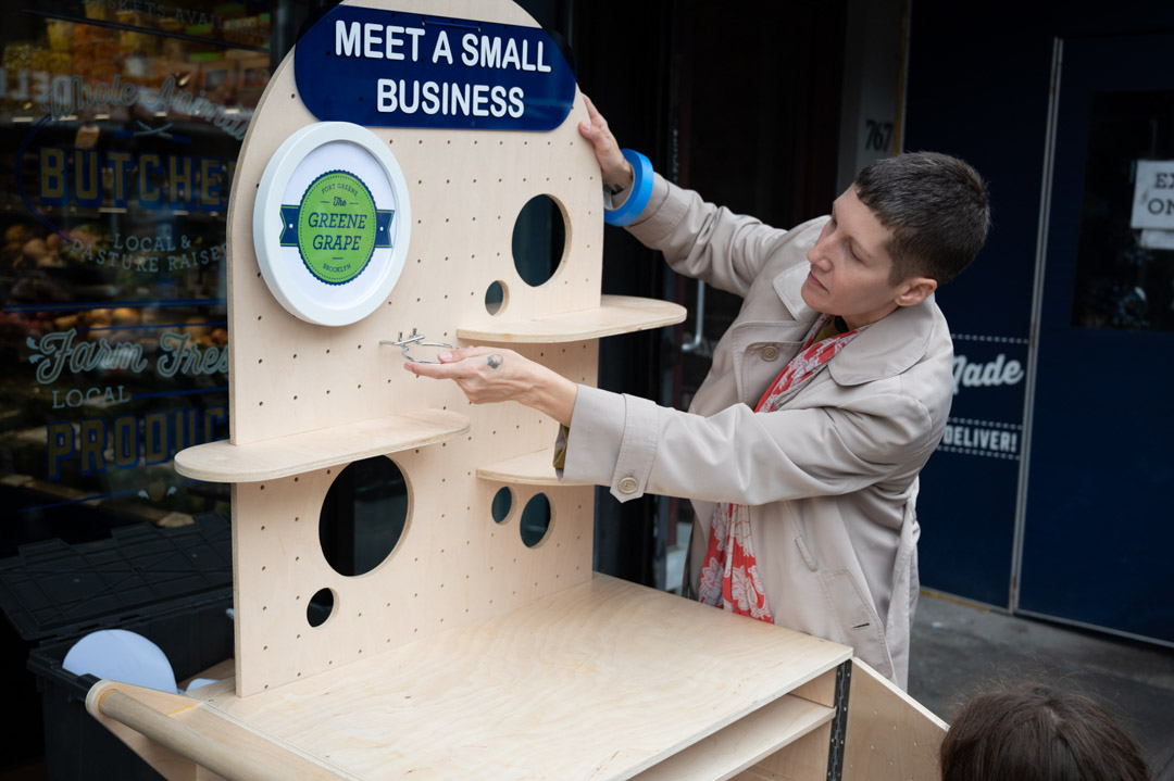 A woman putting a sign "MEET A SMALL BUSINESS" on a wooden cart on the street.