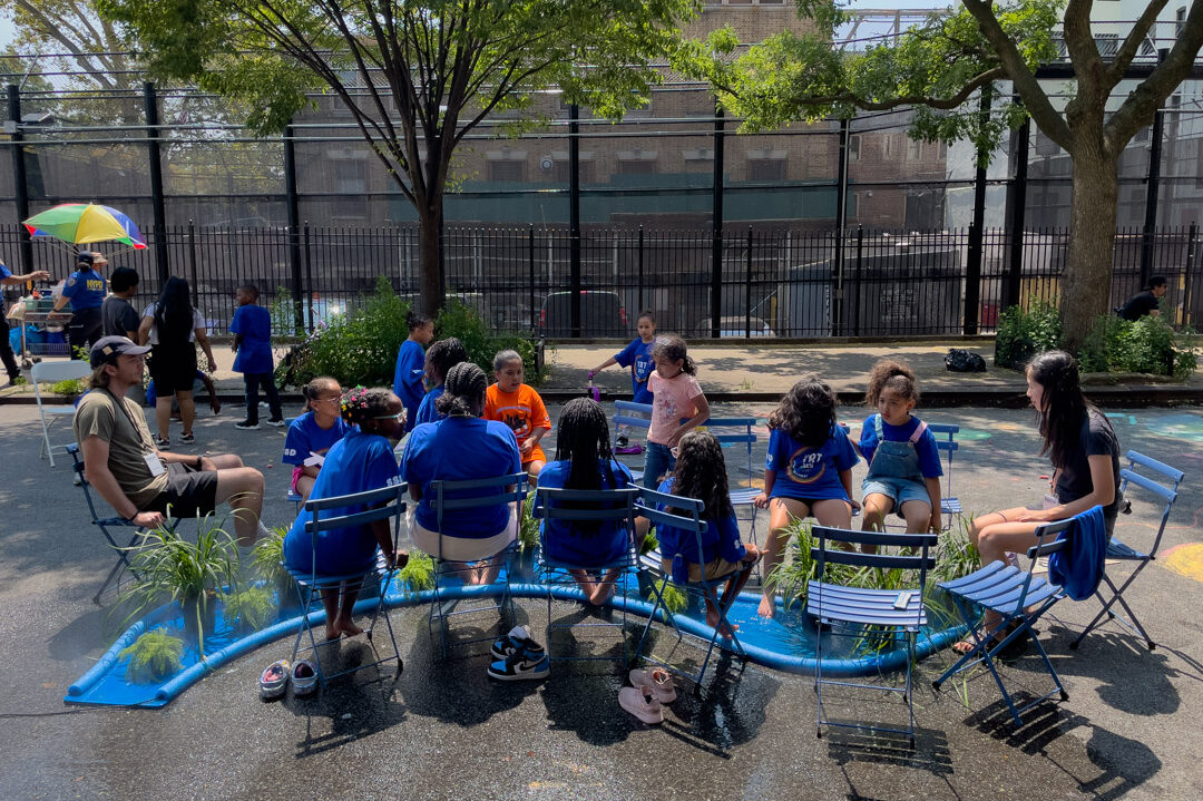 People sitting around a blue, misting river-like structure on the street.