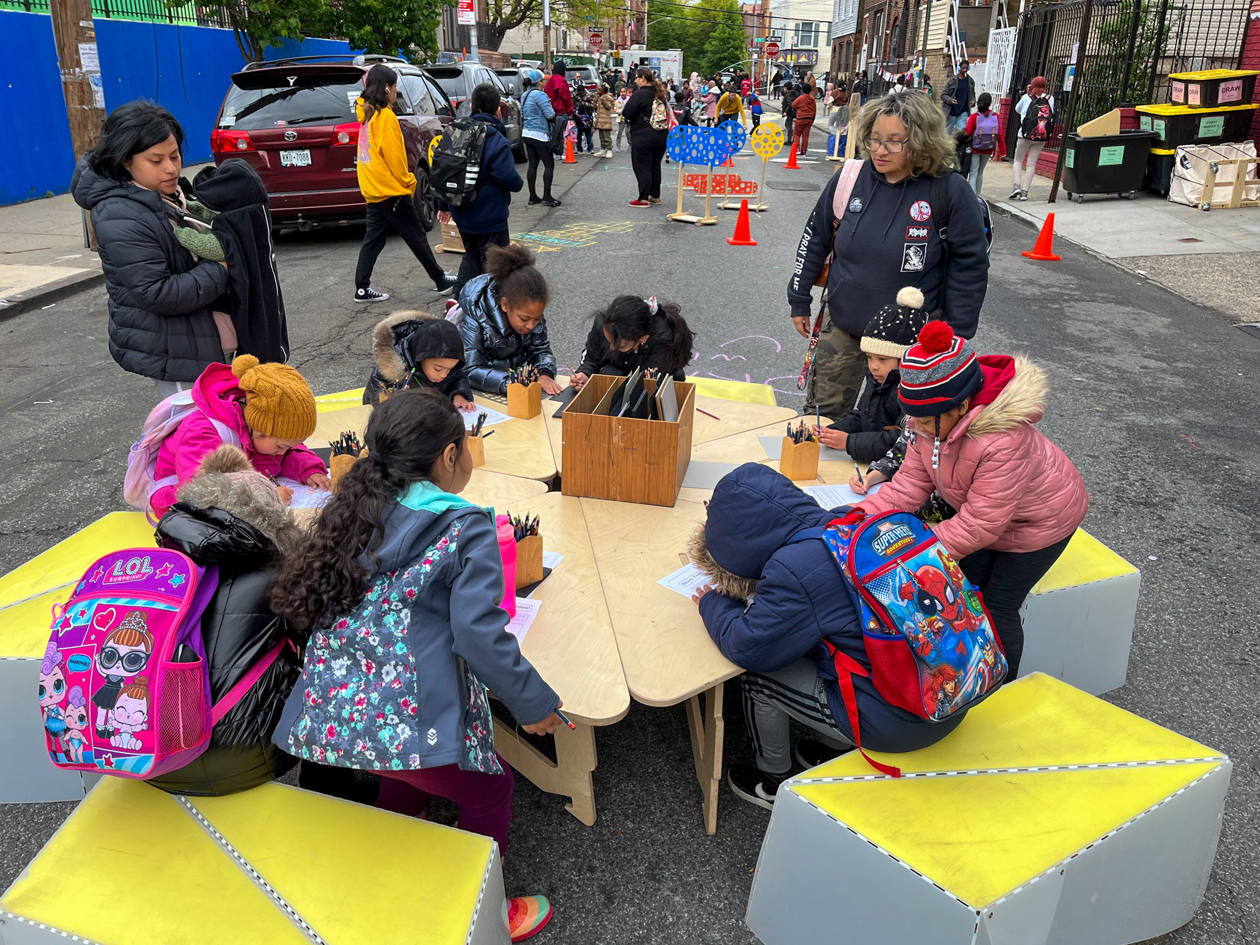 elementary students sitting around a wooden table and plastic benches on a street