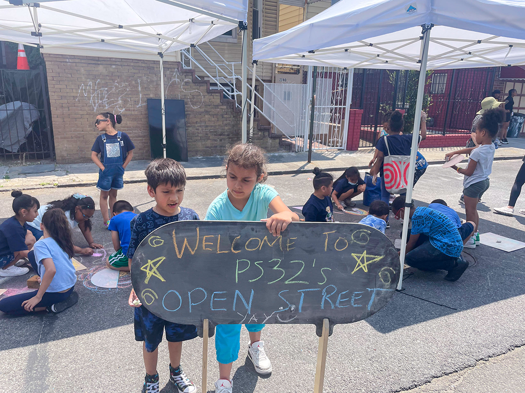 Welcome children on the street with the sign reading "Welcome to PS32's Open Street"