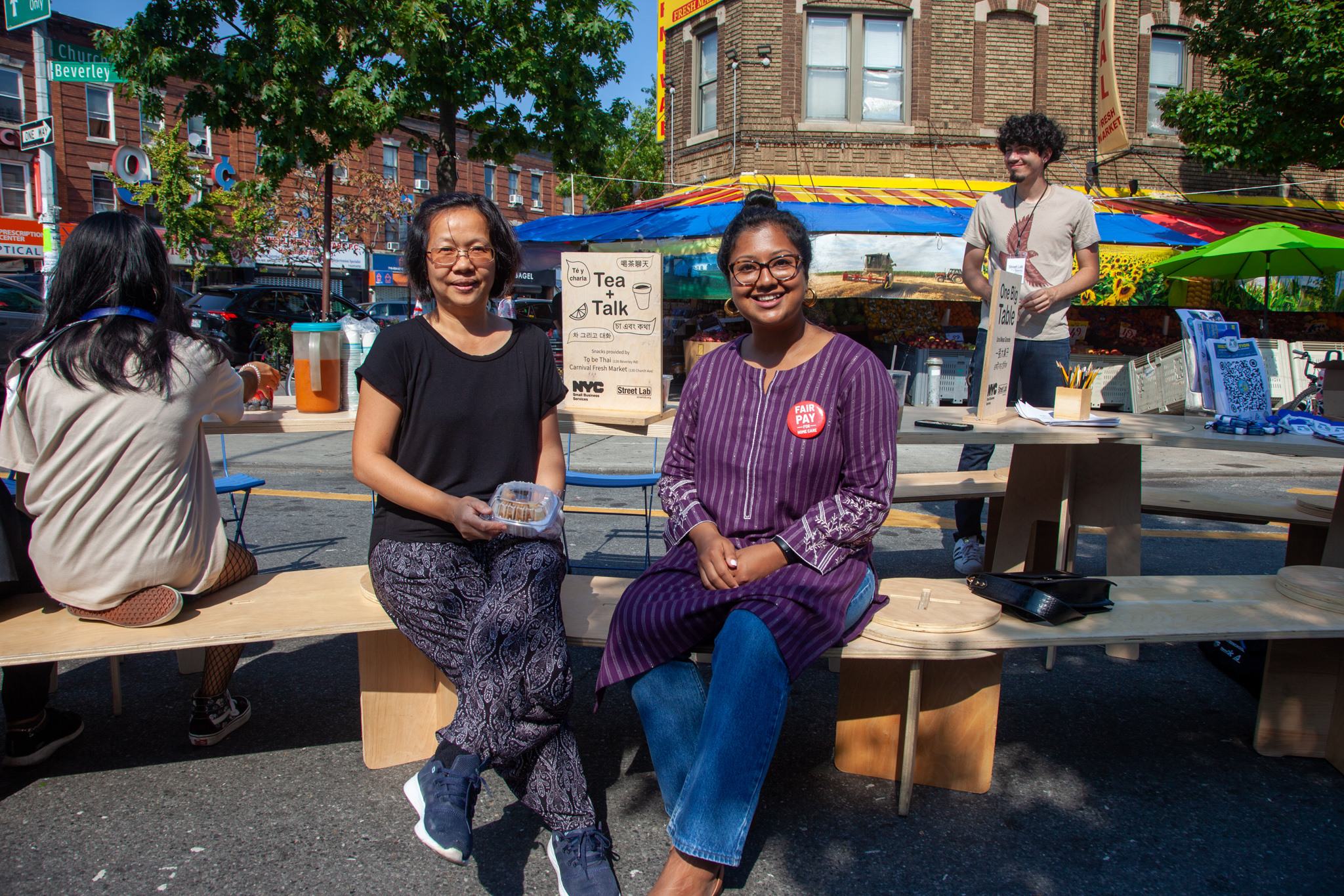 Two women sitting on one big bench by Street Lab on the street.