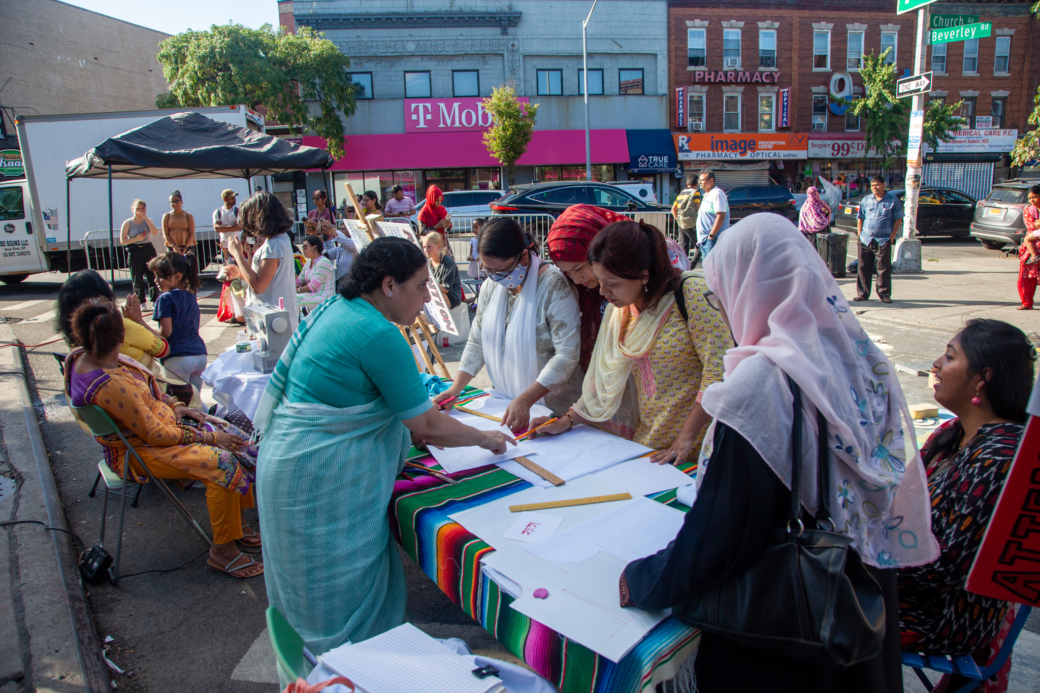 A group of people learning how to embroider on one big table on the street of NYC.