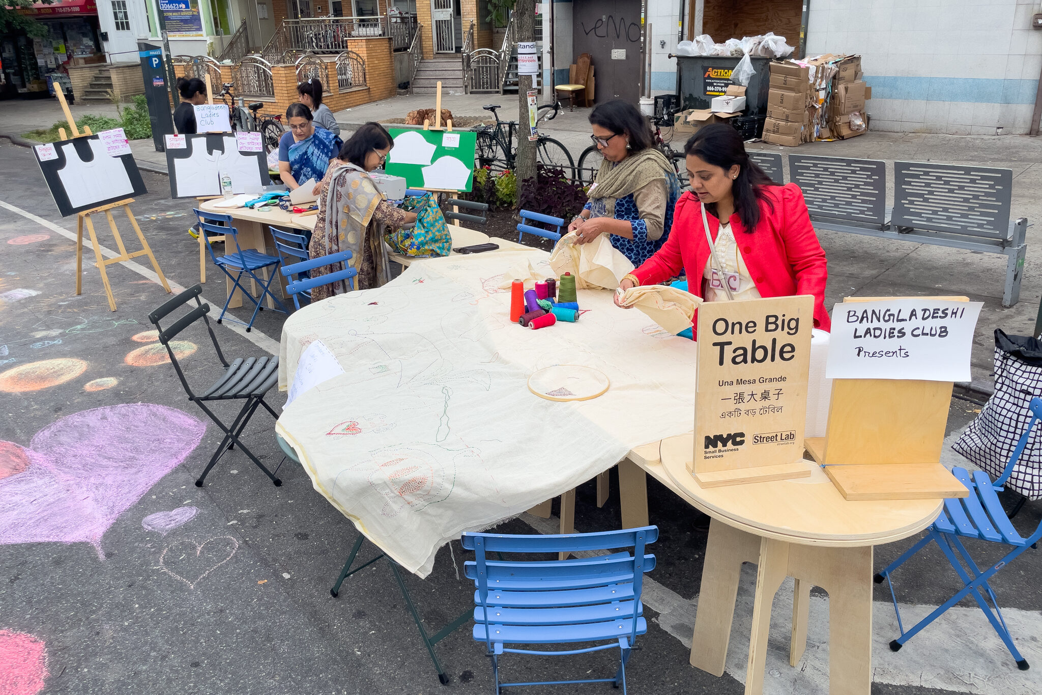 A group of people learning how to embroider on one big table on the street of NYC.