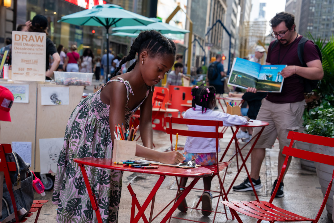 A girl drawing on a red cafe table on a NYC street.