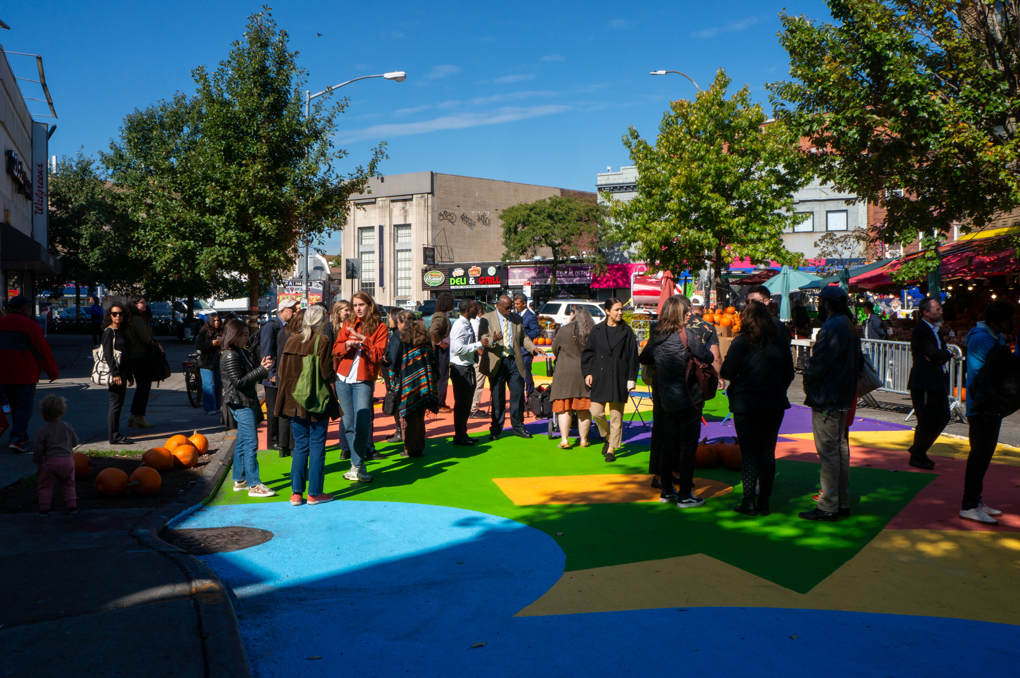 A crowd standing on an open street with colorful mural ground.
