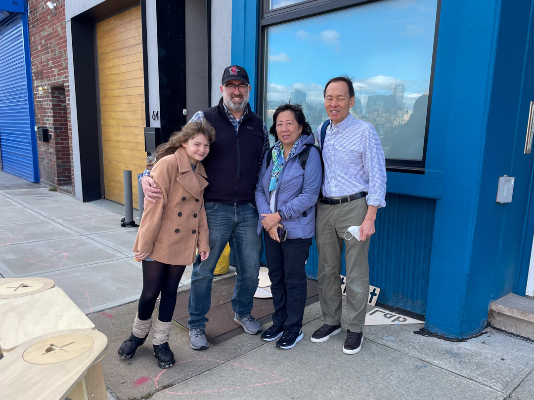 Three adults and a child posing for the camera on a sidewalk.