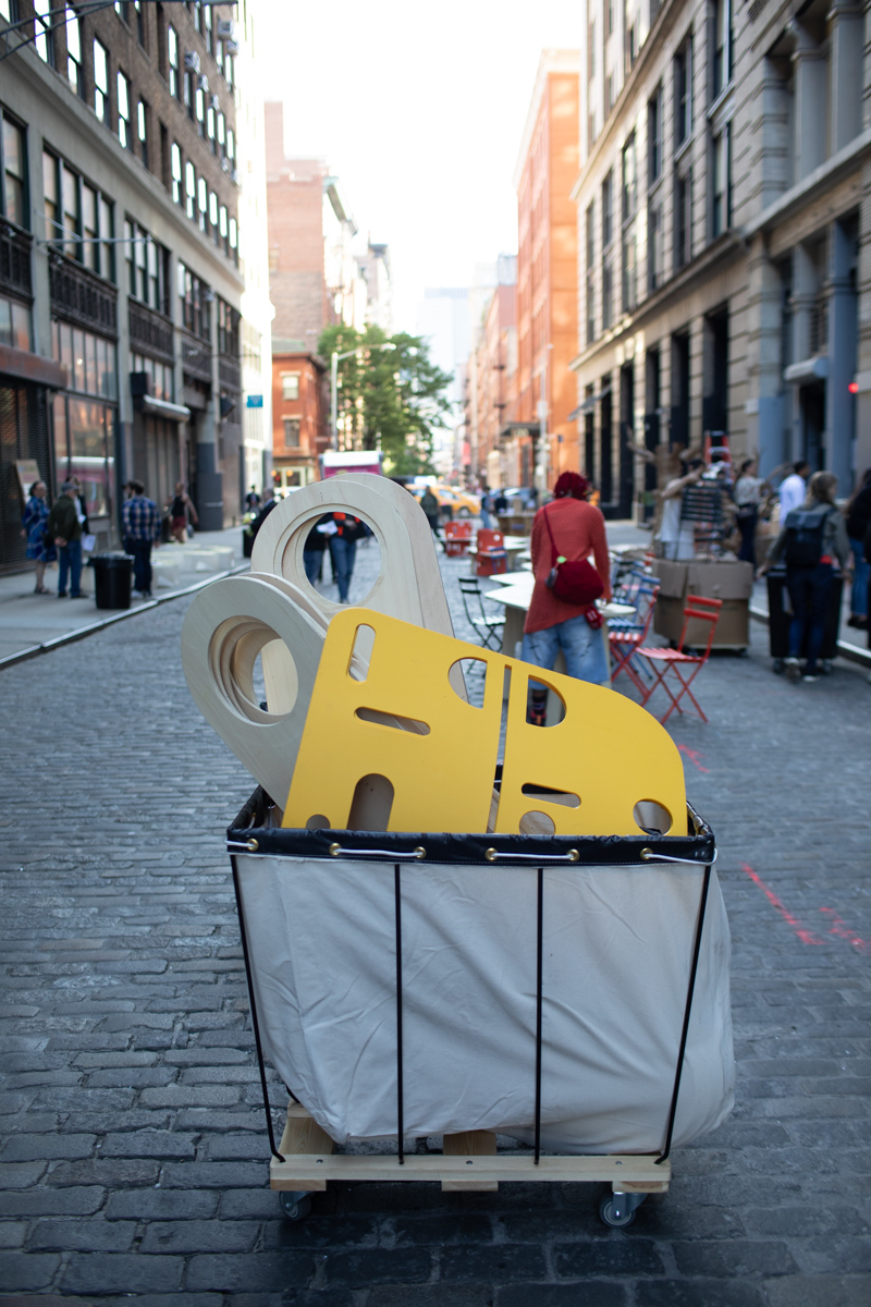 A photograph of plastic and wooden pieces (to make up a portable bench) sticking out from a cotton cart in the street of NYC.