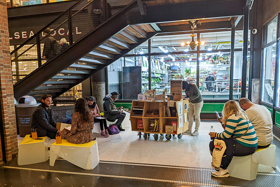 A photograph of people drawing in an indoor marketplace.