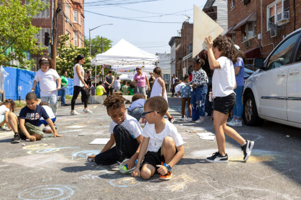 A view of children playing on the street and chalking on the ground. The button on the top right corner reads 