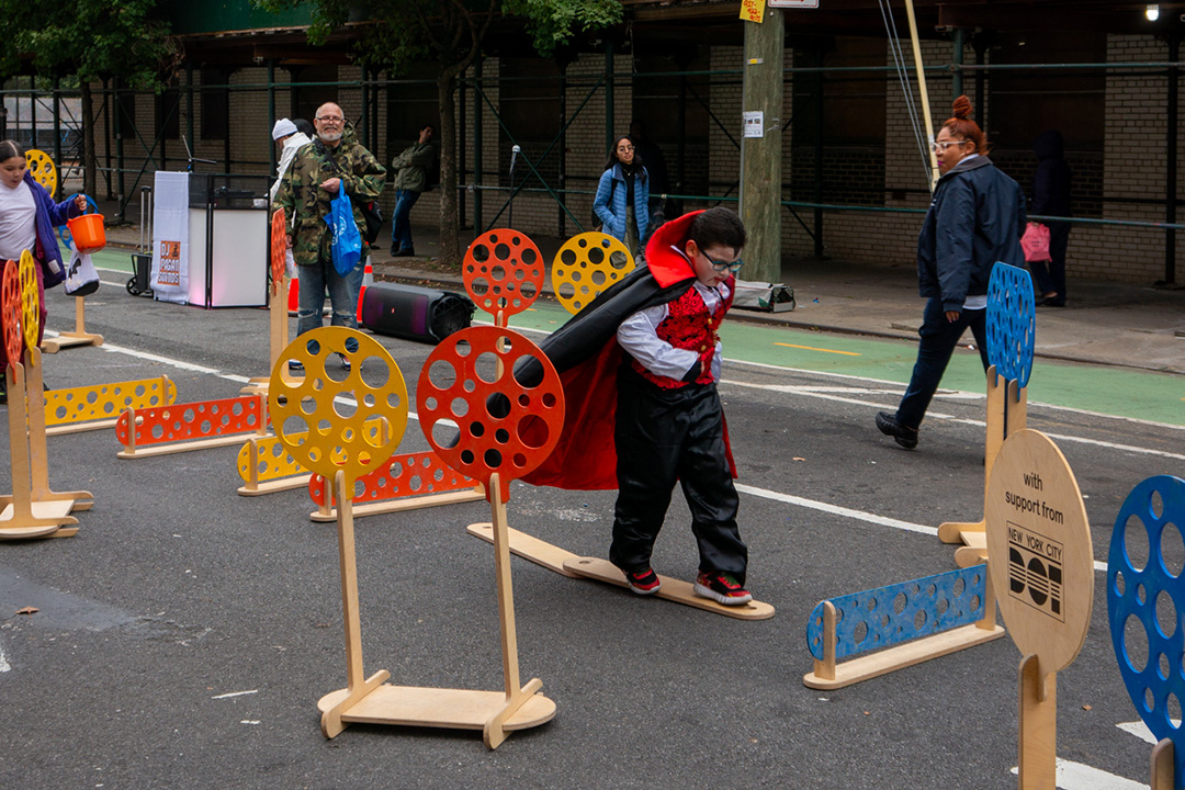 A child dressed up as Dracula for Halloween jumping on hurdles in the street of NYC.