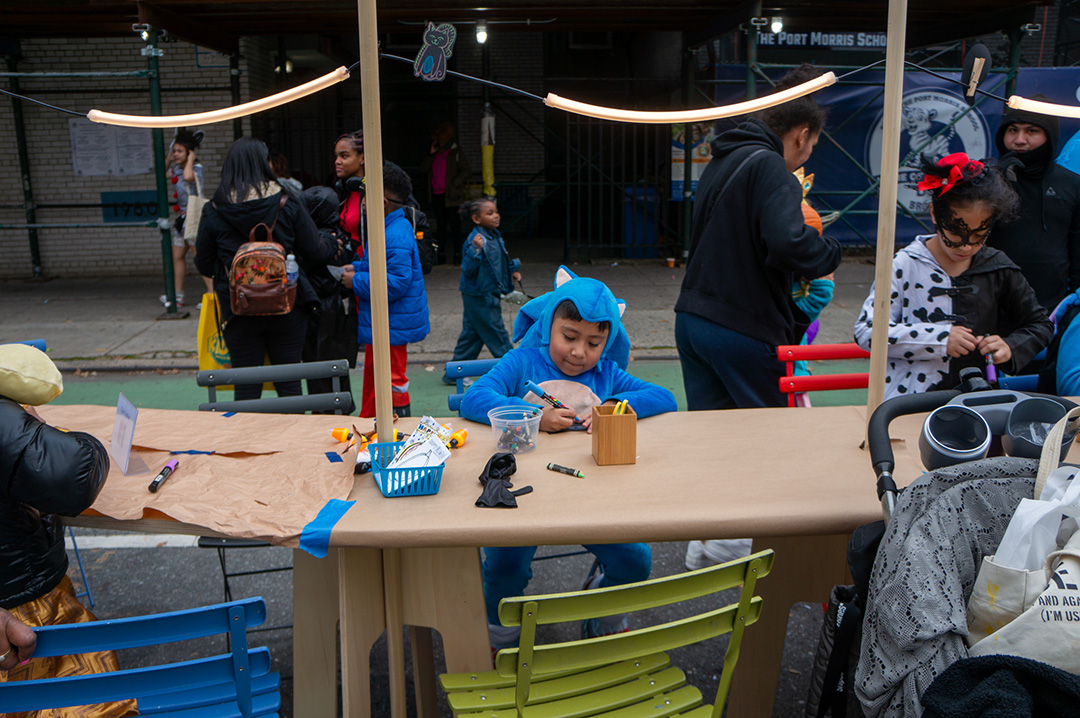 A boy dressed up as Sonic the hedgehog drawing on a Street Lab's One Big Table in the street.