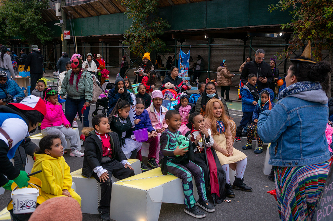 A group of children listening to an adult reading a story book in the street of NYC during Halloween.