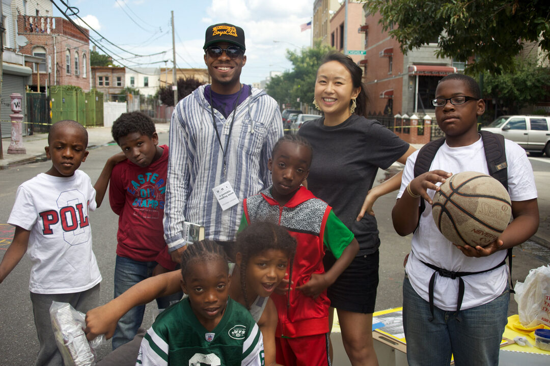 Adults and children smiling and posing at the camera on the street of NYC.