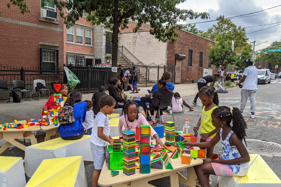 Children playing with magnatiles on the street of NYC, on a triangular wooden table and plastic benches.