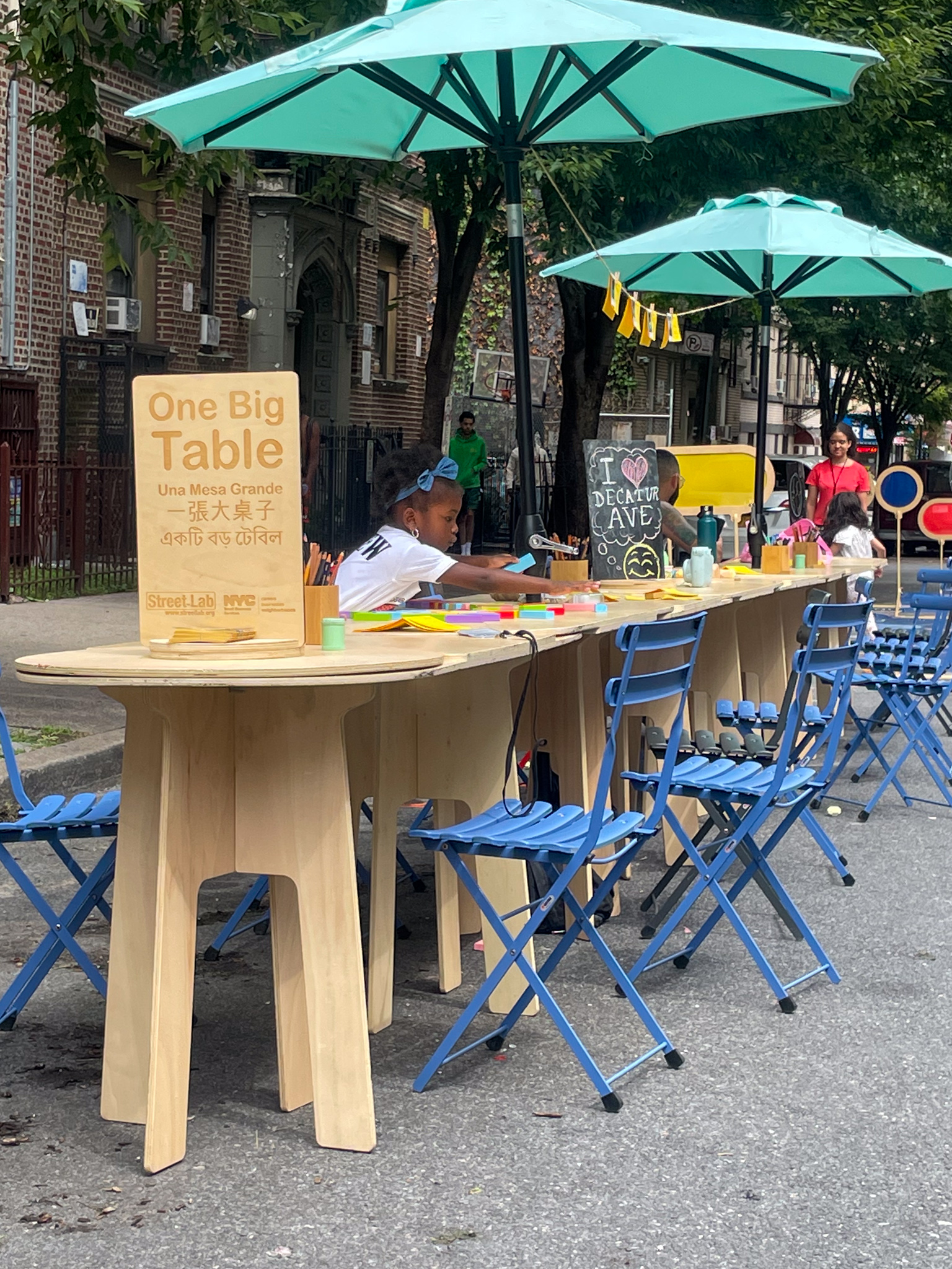 A little girl at a long table outside in a street of NYC.
