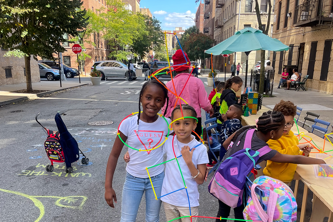 A view of two children smiling with plastic straw toys in their hands on a street in NYC.