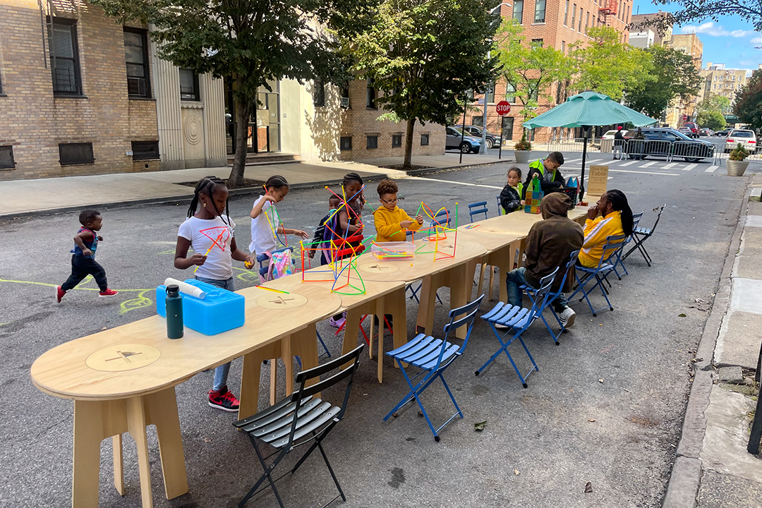 A photo of children playing on a long wooden table on a street in NYC.