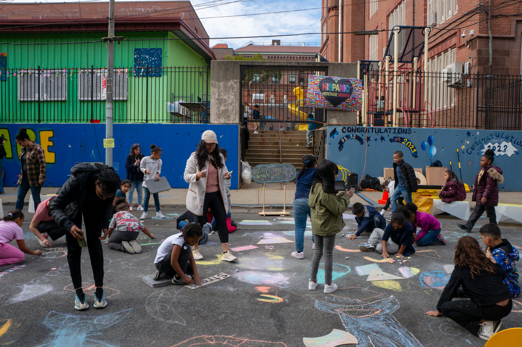 A view of an Open Street with elementary school students and teachers chalking on the ground.