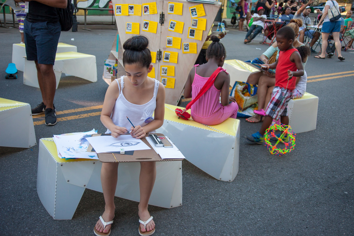 A photo of children in a straight line facing the camera, with colorful play obstacles in front and school building in the back.