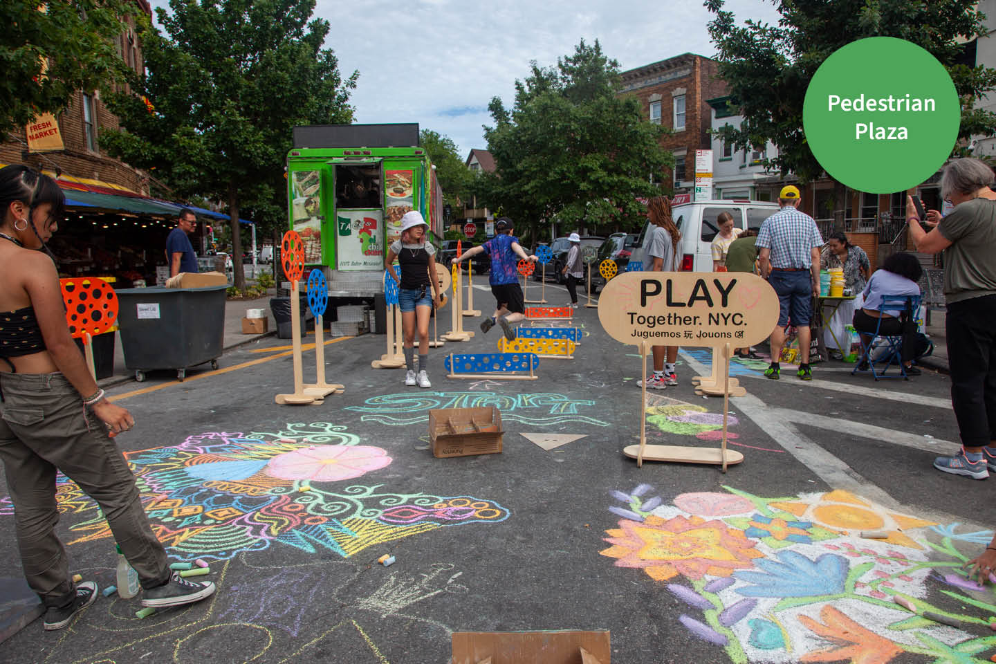 A view of people chalking on the street in NYC. There is sign that says "PLAY." The button on the top right corner reads "Pedestrian Plaza."