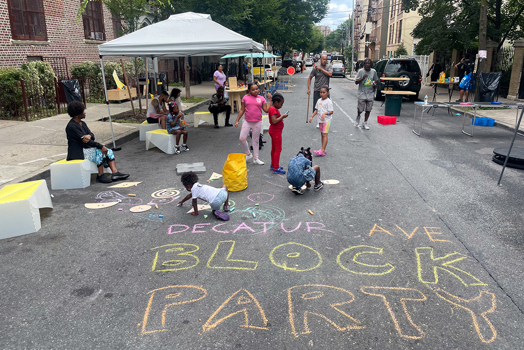 A view of a car-free open street. The chalked text on the street reads "DECATUR AVE BLOCK PARTY"