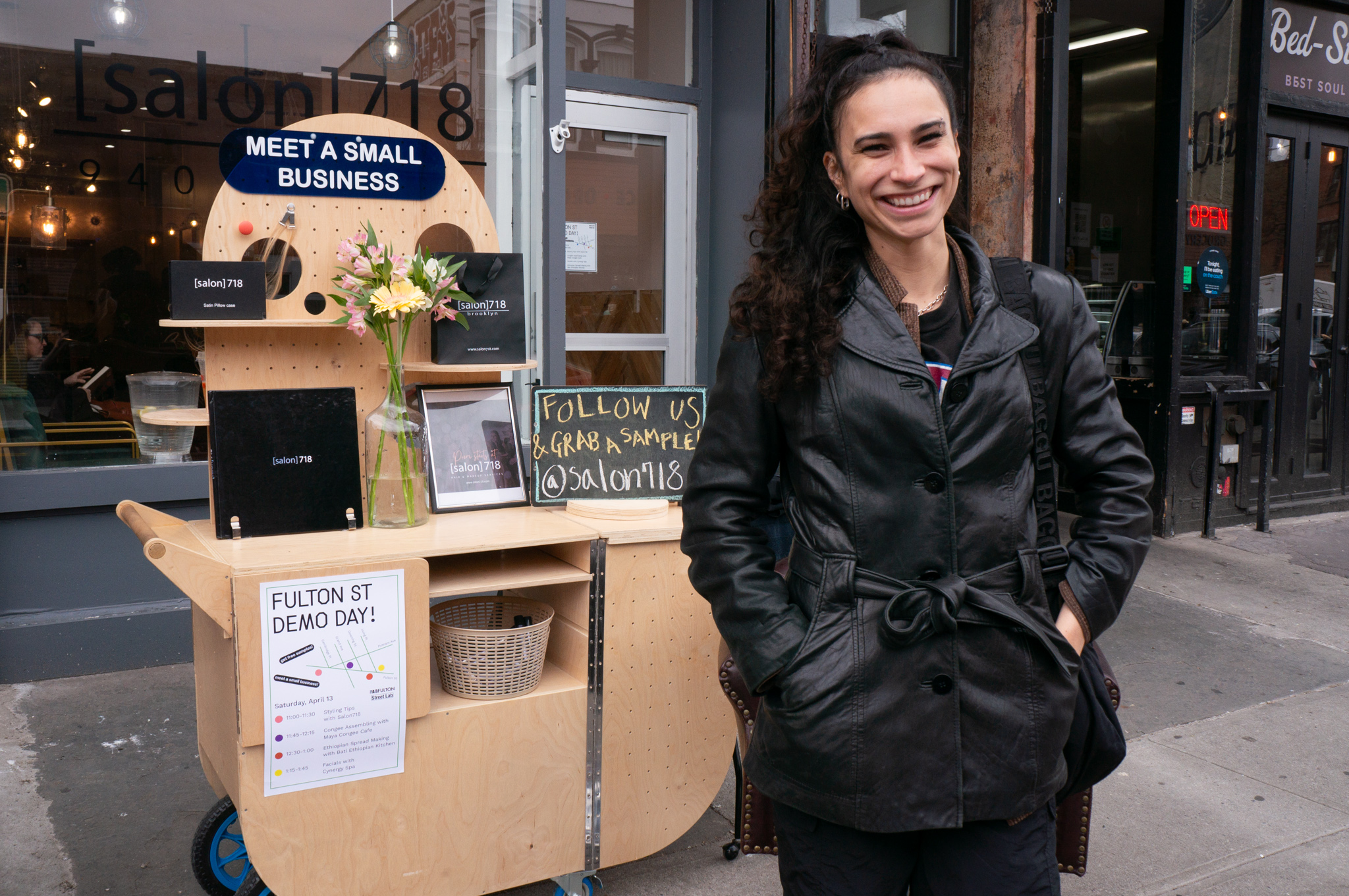 A woman smiling in front of a wooden cart on the street.