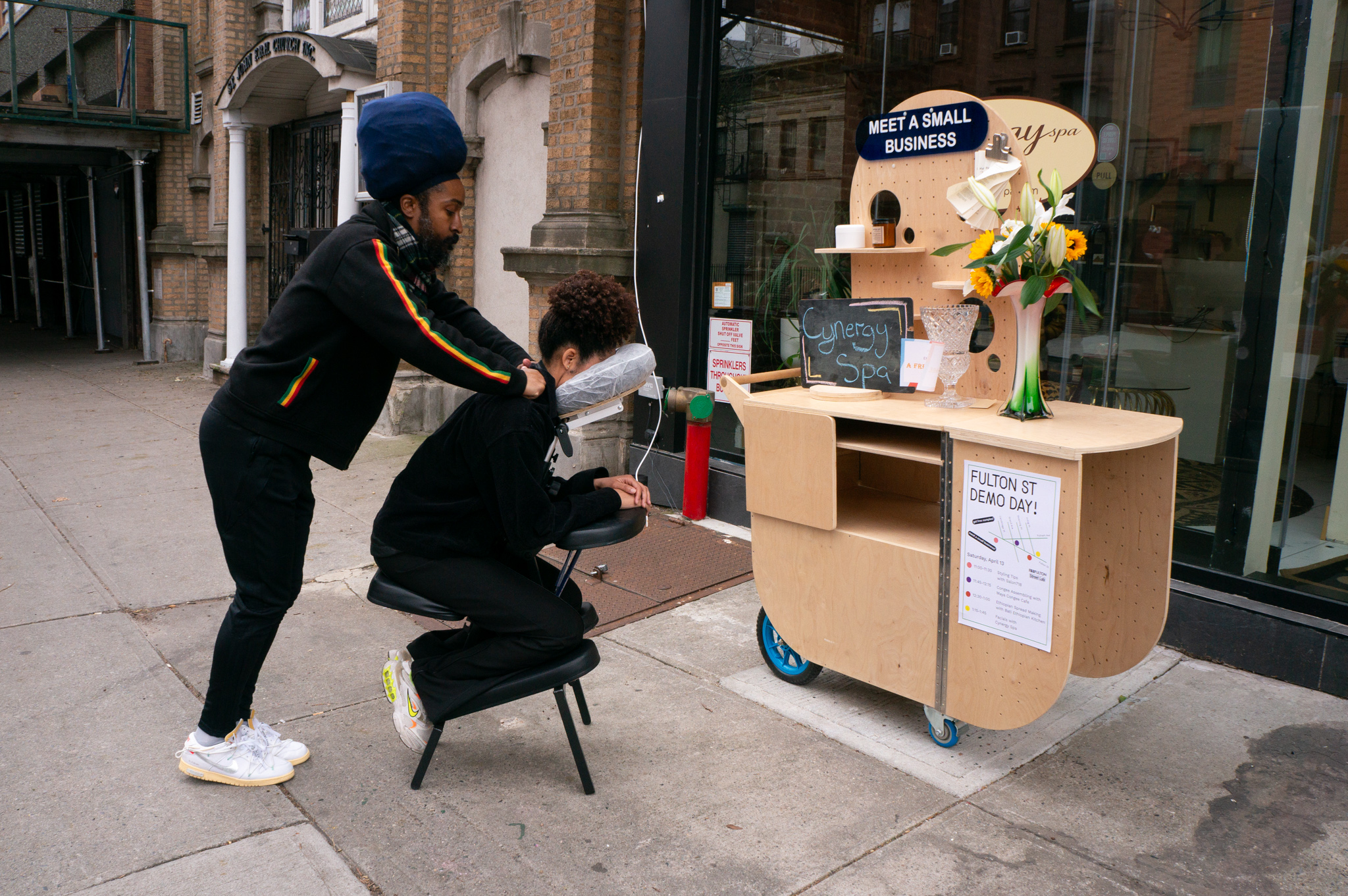 A masseur demonstrating a massage session on the street in front of the storefront.