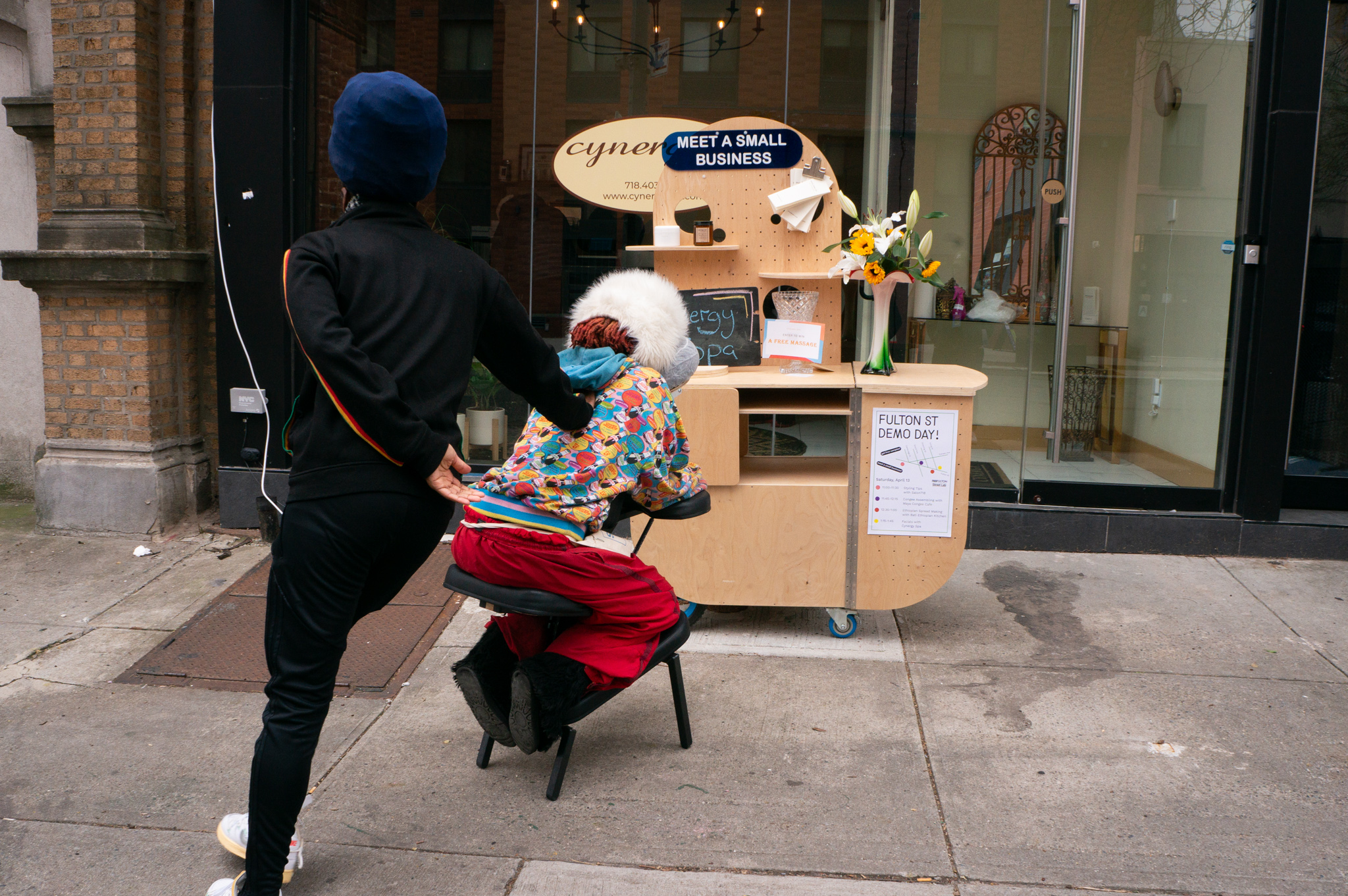 A masseur demonstrating a massage session on the street in front of the storefront.