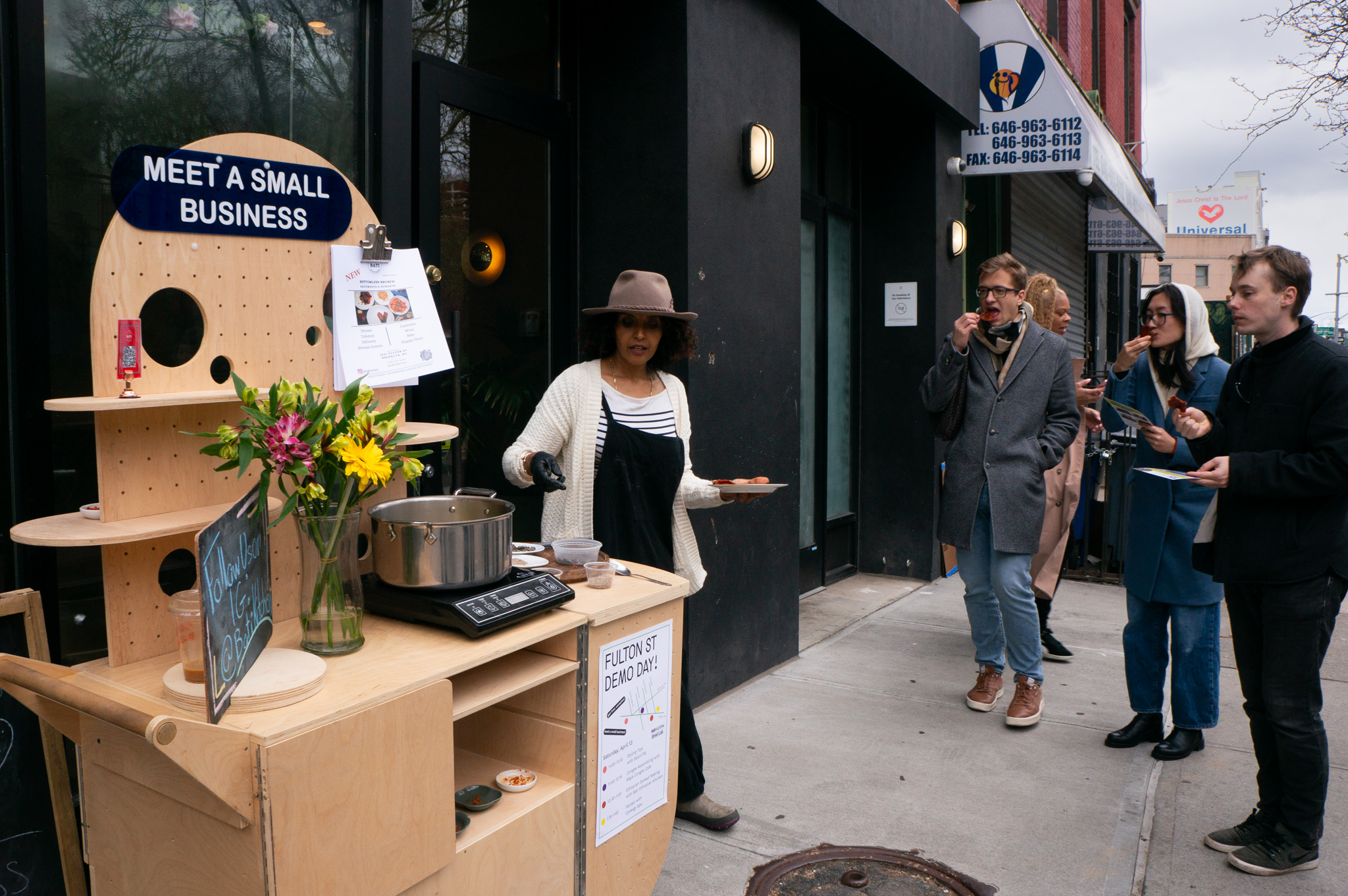 A restaurant owner showing different spices to people on the street with a wooden cart.