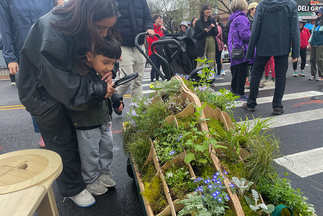 A woman and a little boy looking at a cart full of plants on the street.