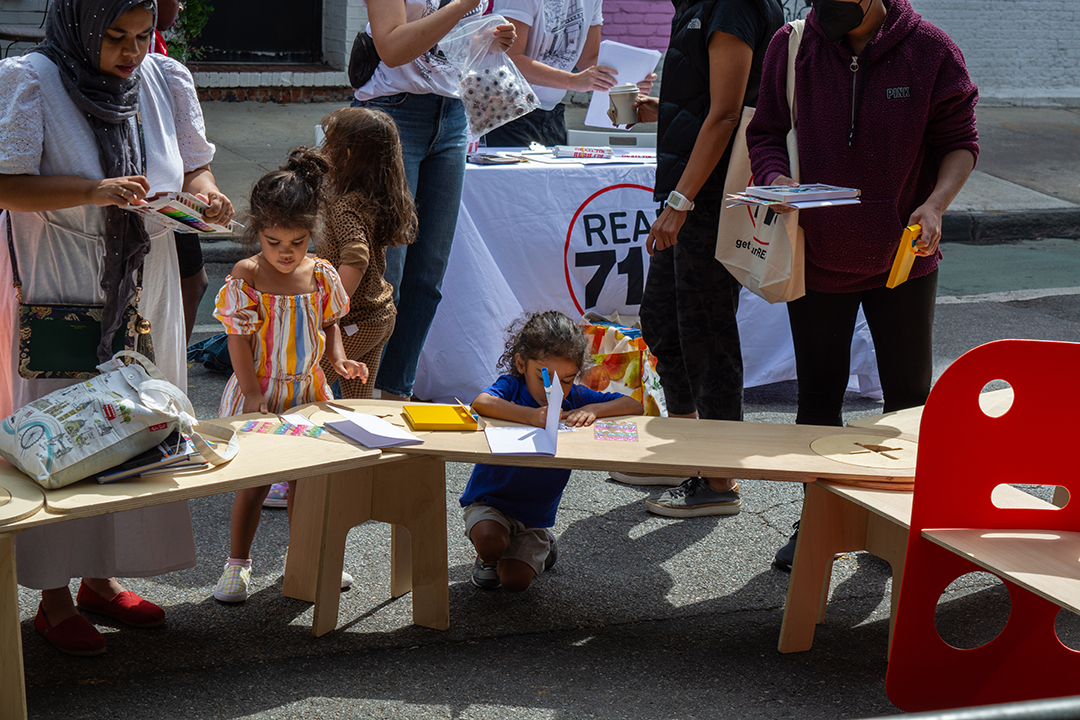 A little girl drawing something on a wooden bench on the street.