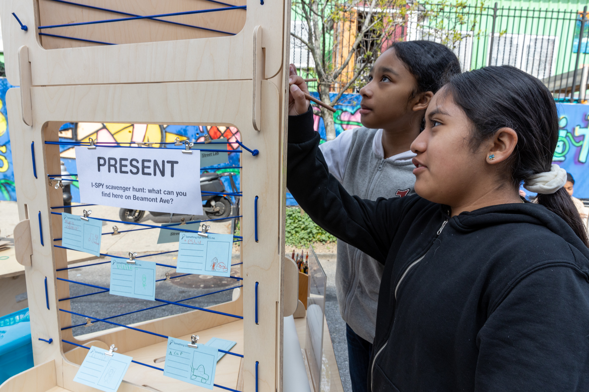 Two girls writing something on notecards clipped on the wooden frame.