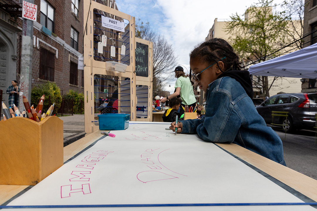 A boy writing something on the roll of paper on a wooden table on the street.