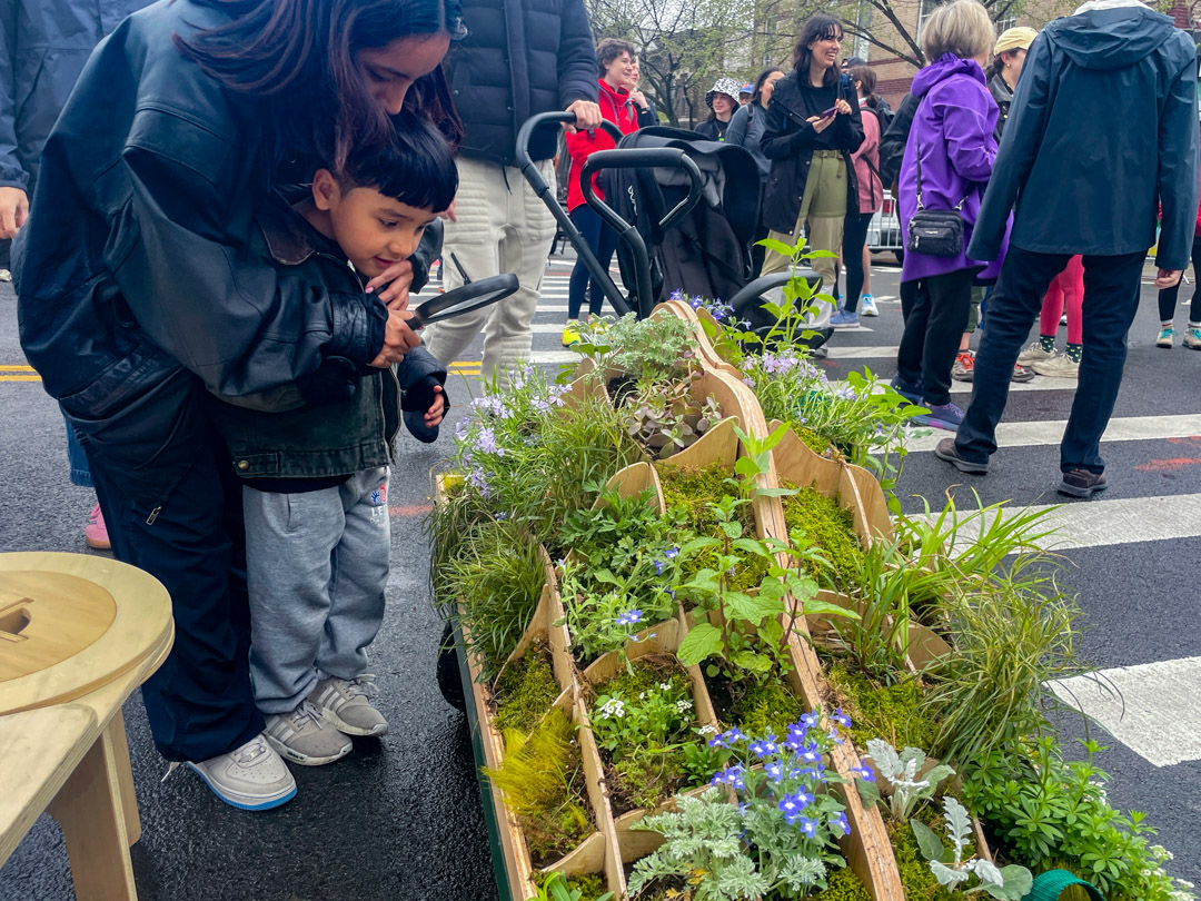 10_2024-04-20-104734_5ave_40st-41st_sunsetpark_1080px A woman and child looking at plants in a cart.