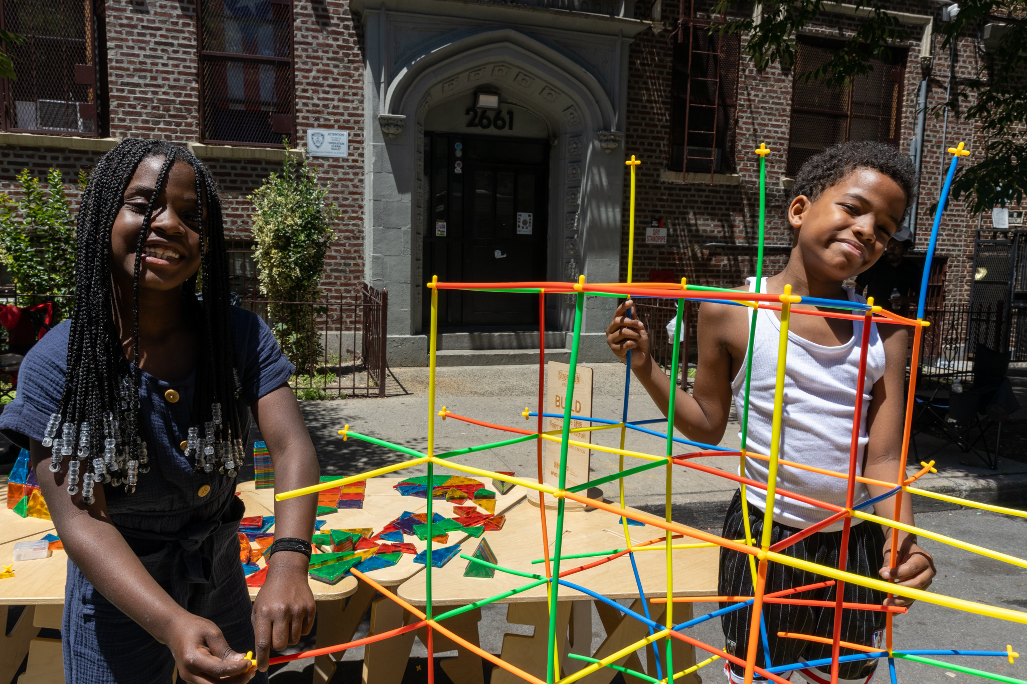 Children playing with straw building structures on the street.