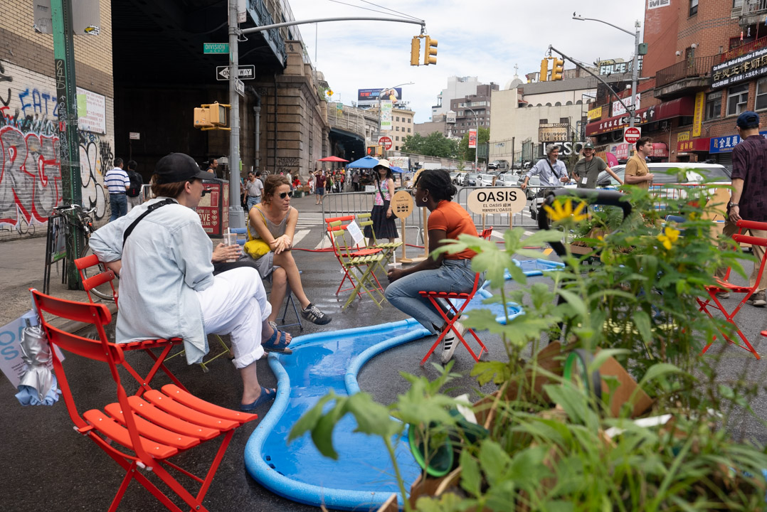 People sitting around a blue, river-like misting structure on the street.