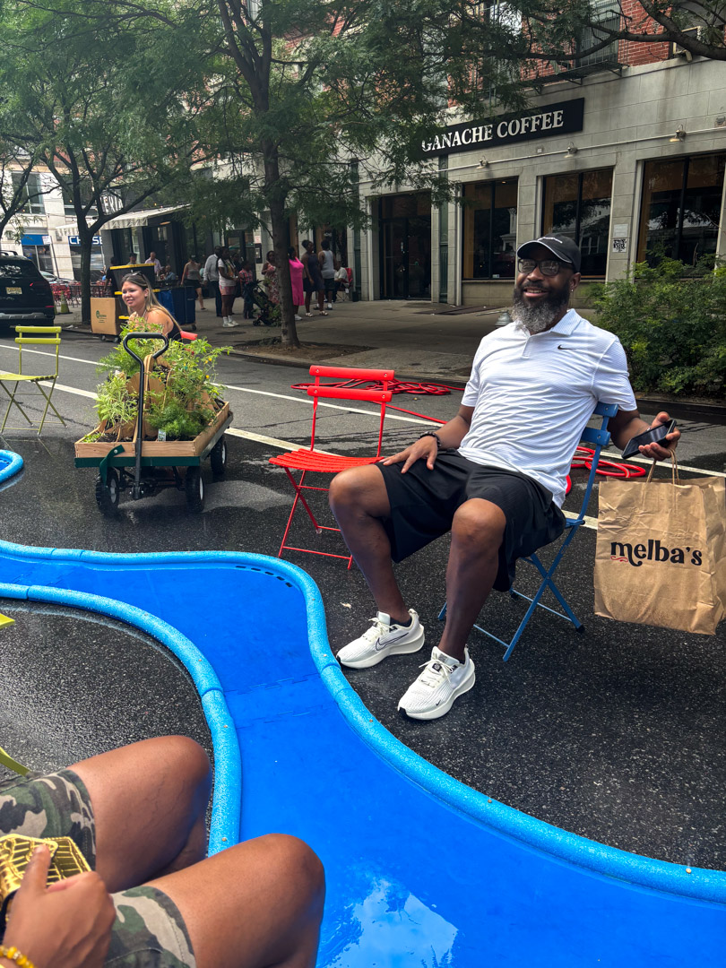 Two people sitting next to a blue river-like misting structure on the street.