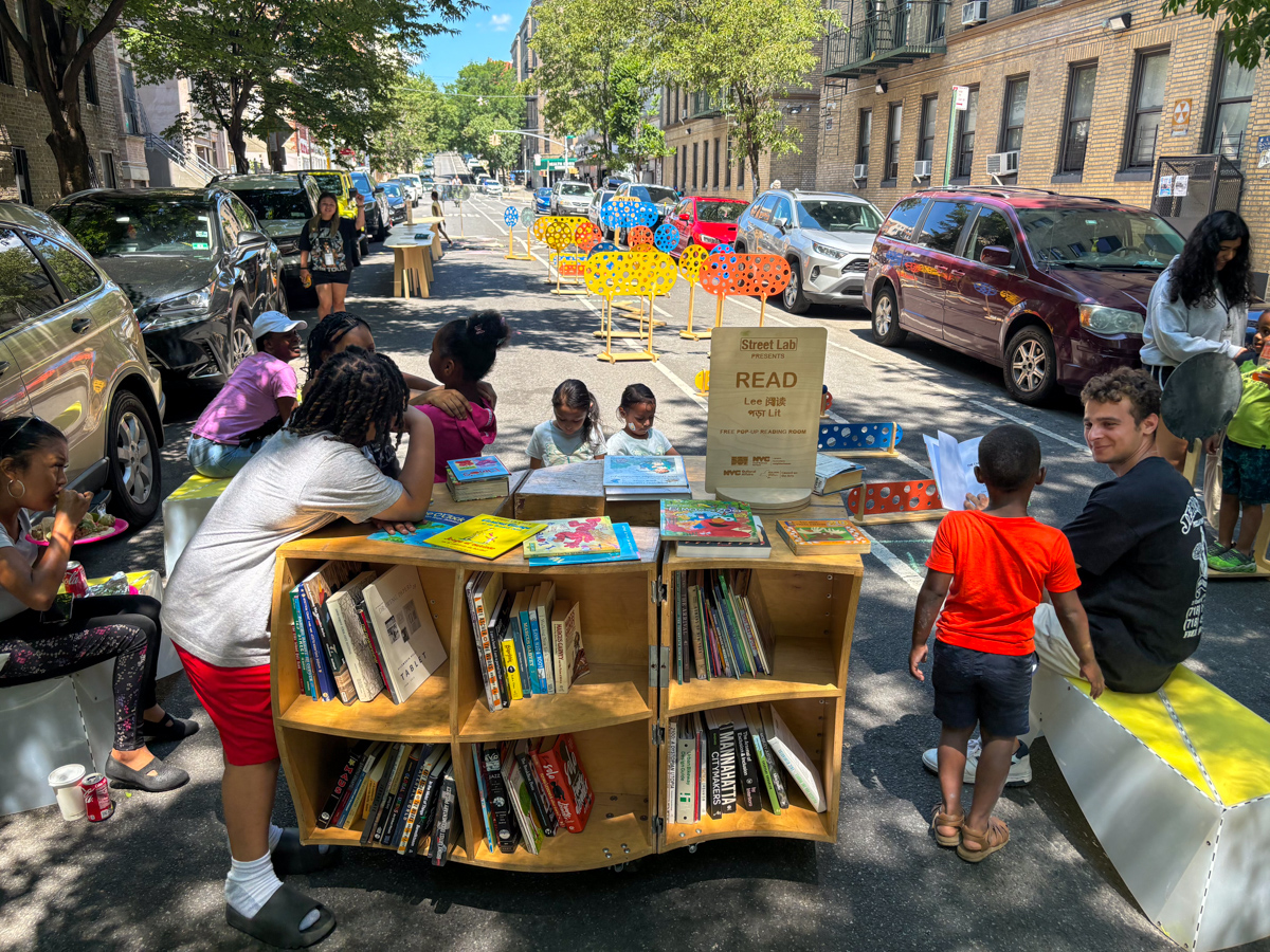People spending time on the street; a wooden reading cart in the foreground.
