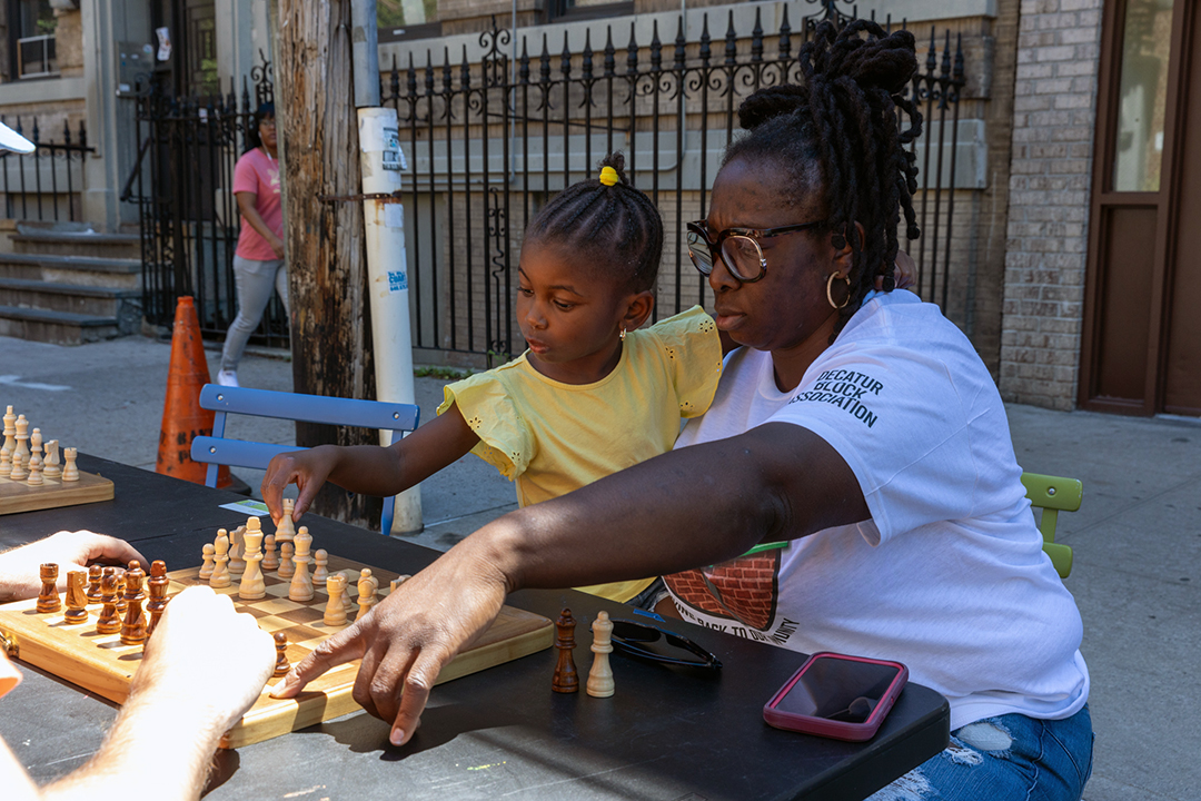 An adult and a child playing chess on the street.