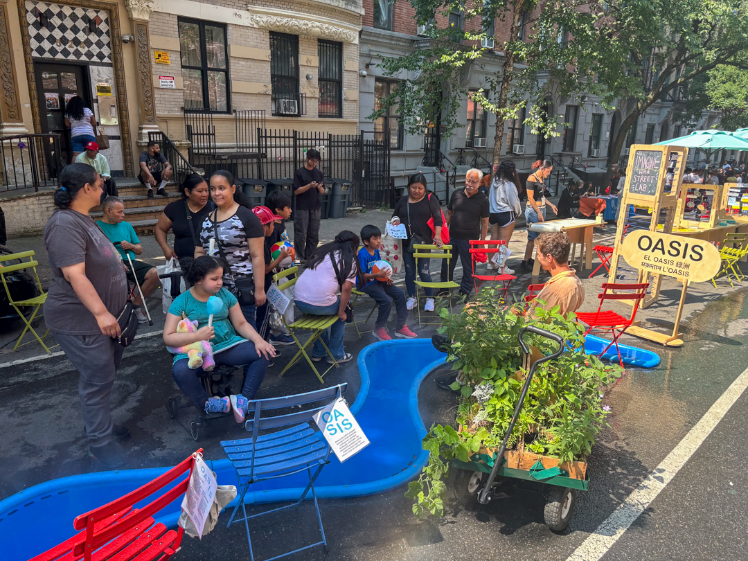 Adults and children hanging out around a blue foam river-like structure on the street.