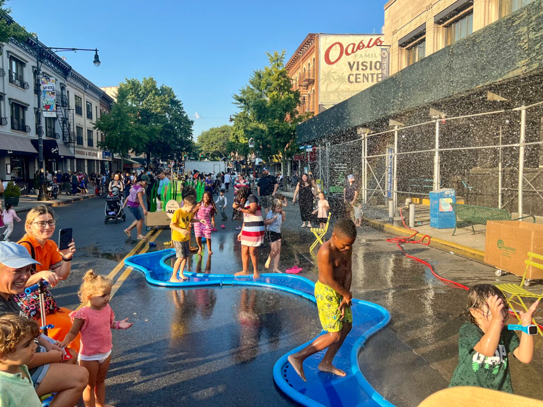 Children playing on a blue, river-like foam structure on the street.