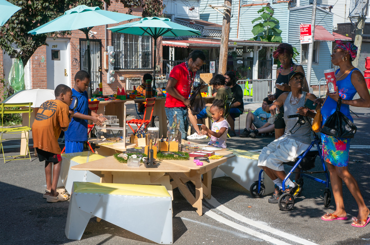 People spending time on the street; a wooden reading cart in the foreground.