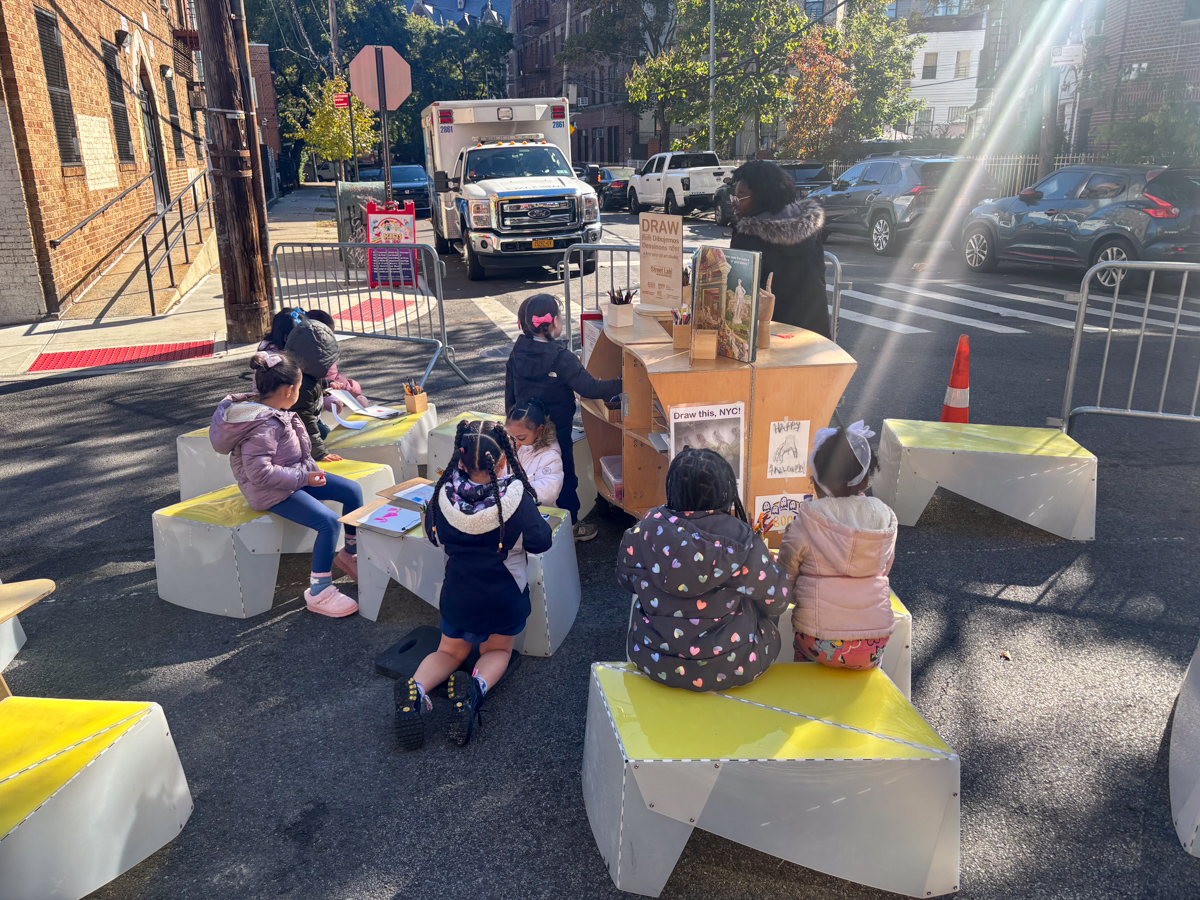 People spending time on the street; a wooden reading cart in the foreground.